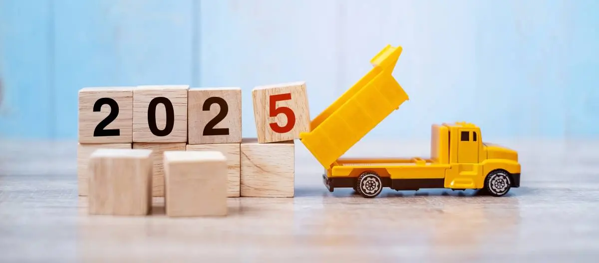a yellow construction truck dumping blocks that spell out 2025