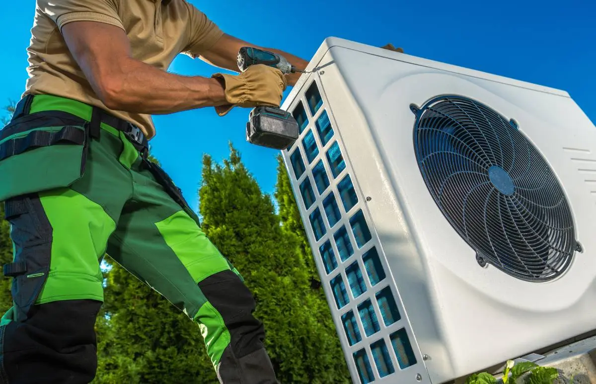an HVAC contractor wearing green work pants and a tool belt, holding a power drill for an HVAC system install