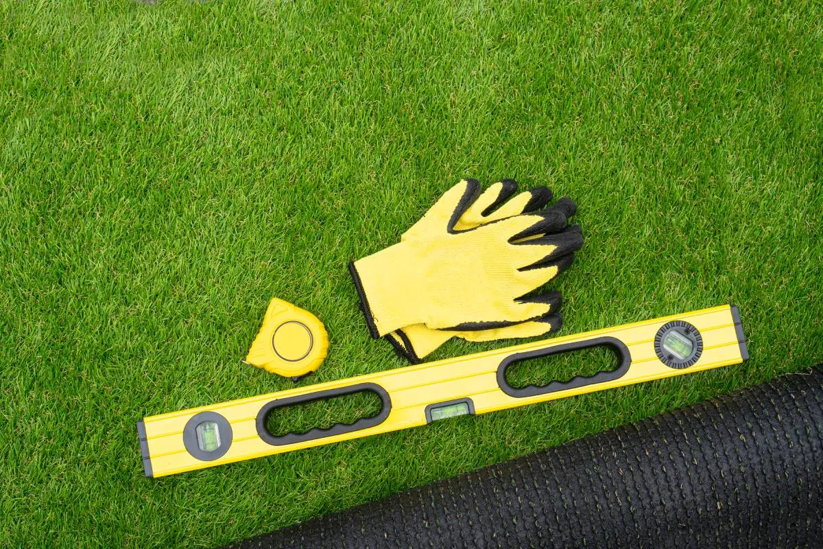 yellow work gloves, level, and tape measure on artificial turf installation 