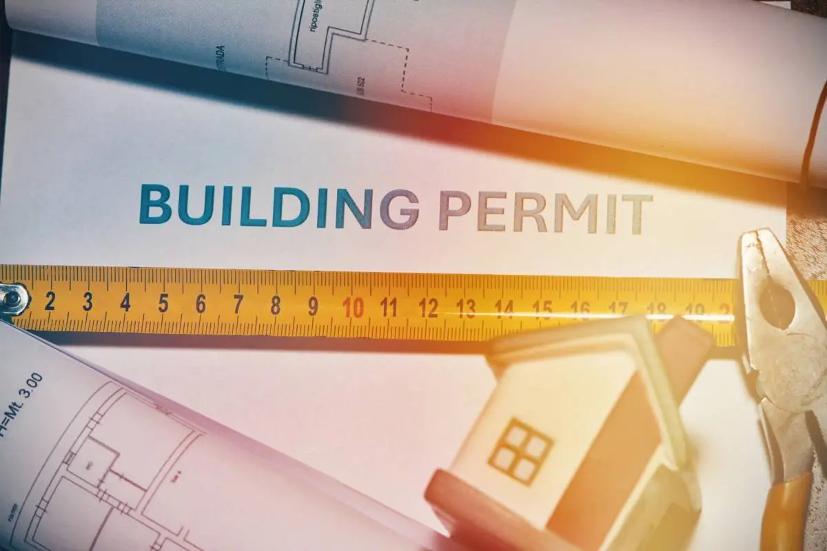 blue prints and building permits laid out with a tape measure, pillars, and figurine of a house