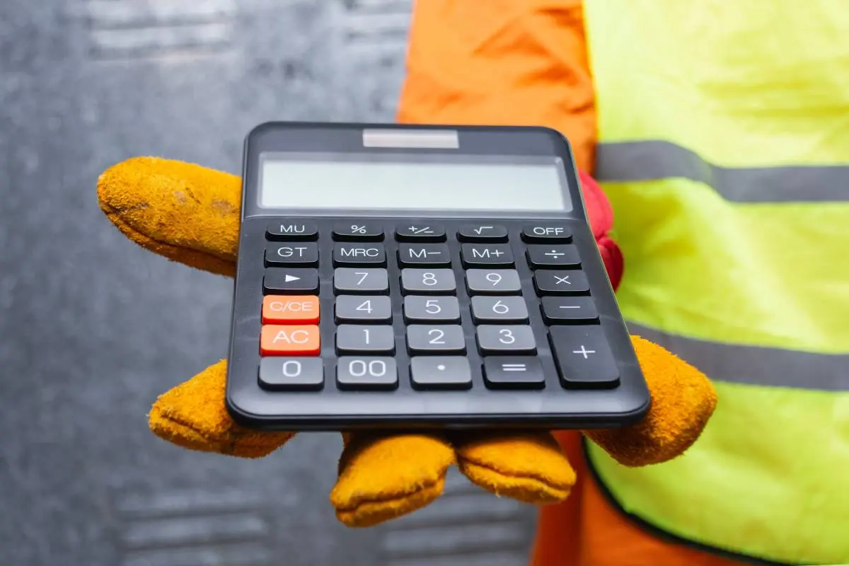 a contractor in a yellow safety vest and safety gloves holding out a calculator