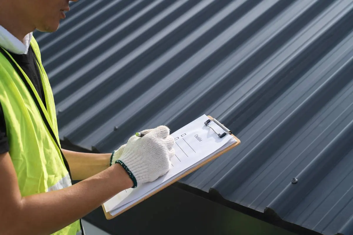 a contractor in a yellow vest going through a checklist as he inspects a roofing project
