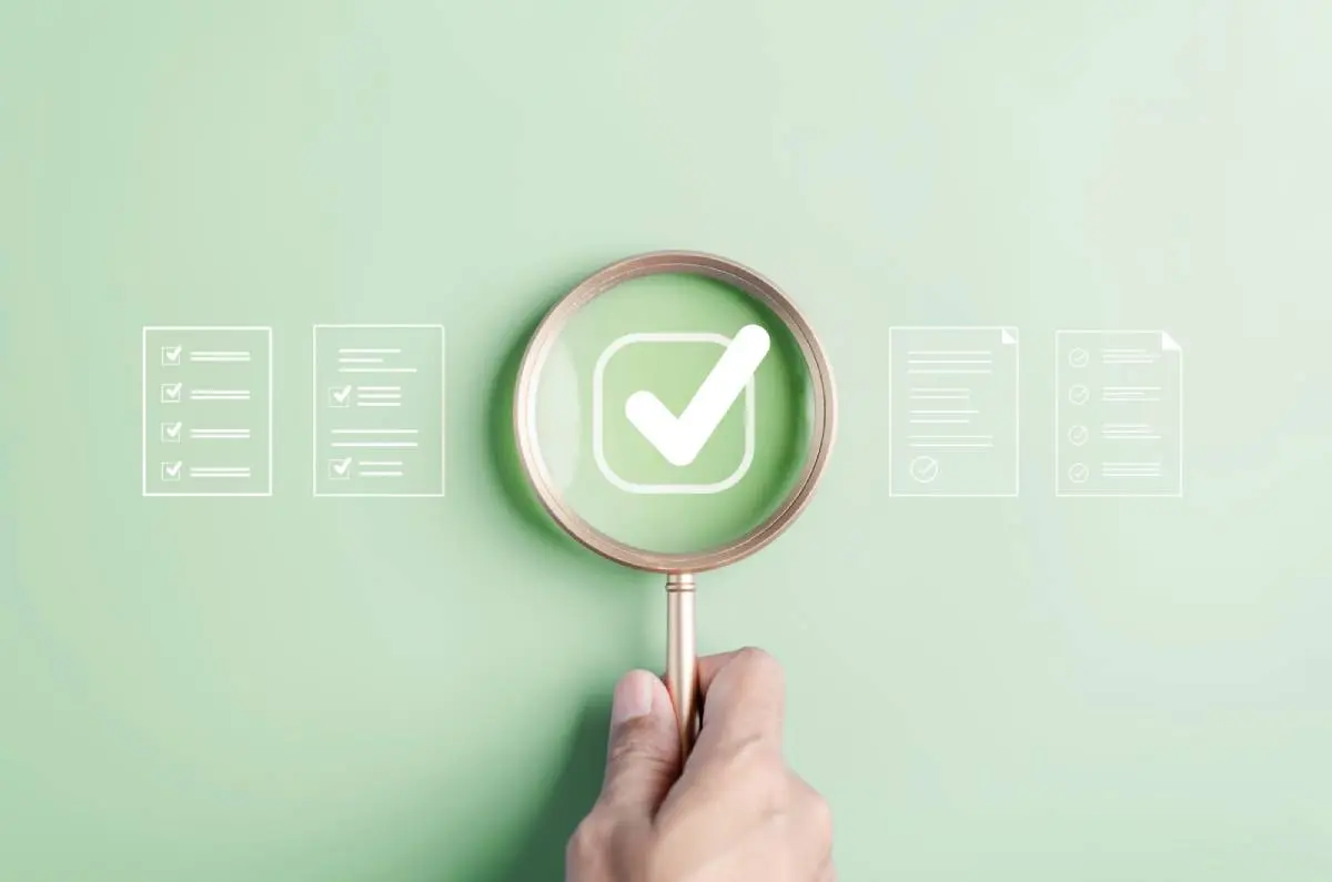 a contractor compliance checklist with documentation under a rose gold magnifying against a light green background