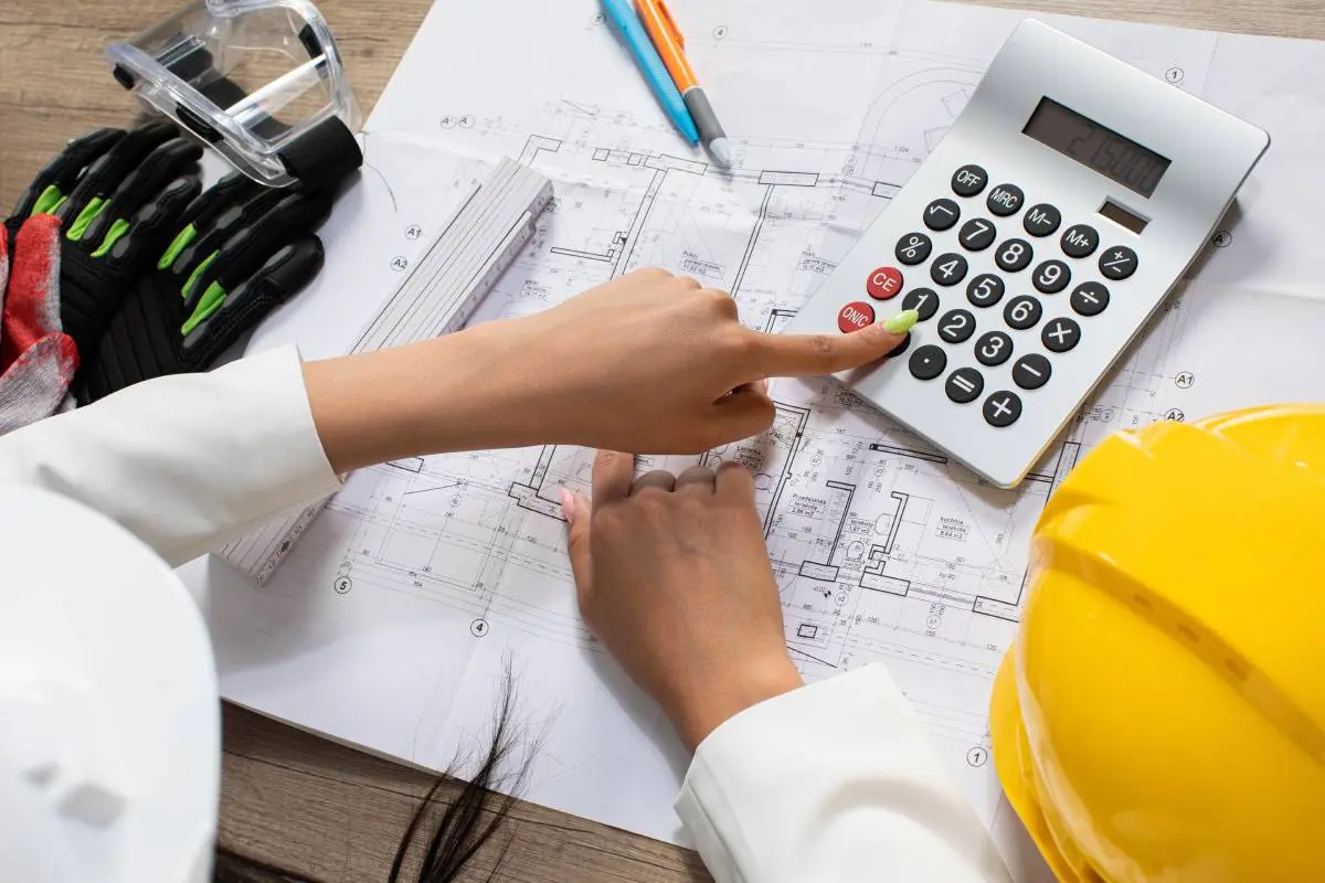 a women with a green manicure looking over a blueprint with a calculator and a hardhat as she creates a cost estimate for a project