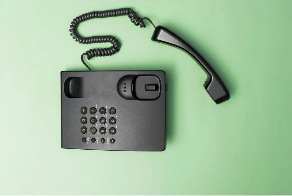 a black corded phone with the receiver off the hook laying on a green background