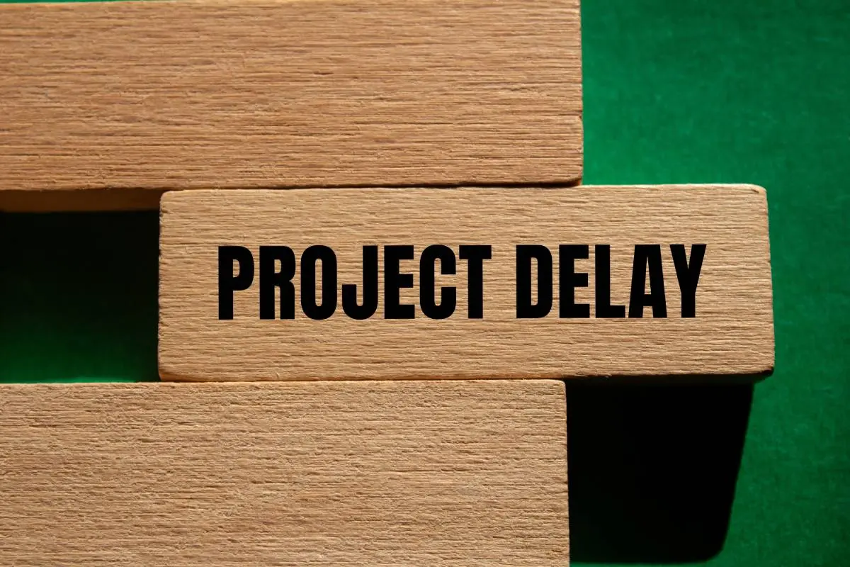 a green felt background with three wooden blocks, the middle of which says "project delay" in black, bold font