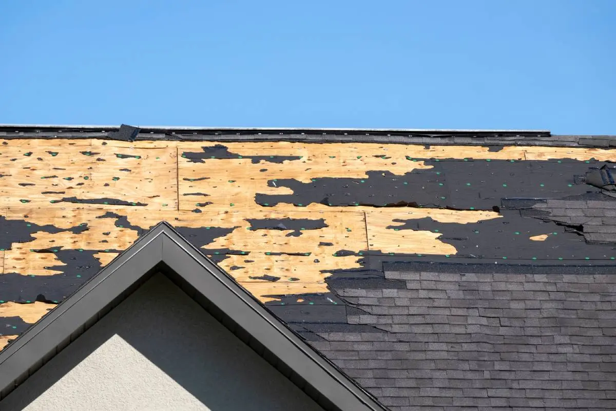 a damaged gray roof in need of emergency roofing repairs with a blue sky behind it
