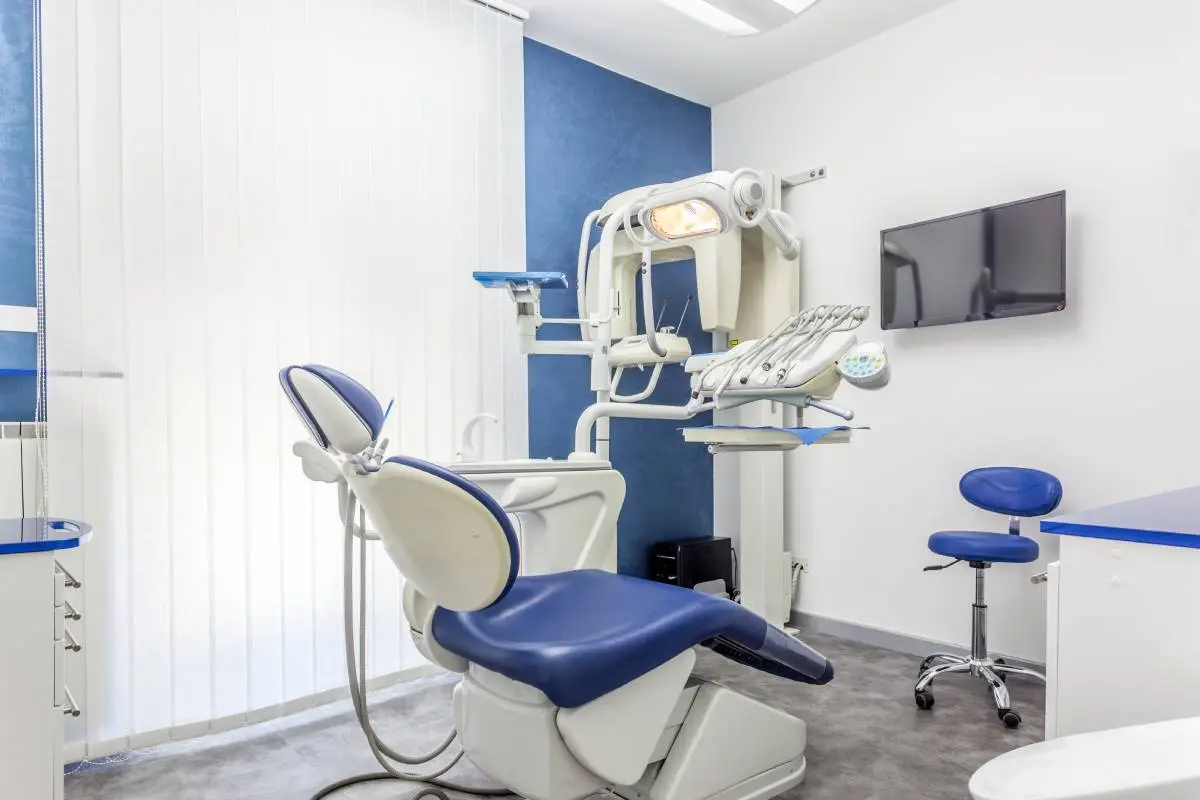 a dental practice office with a blue patient seat and dentist stool, blue walls, and large, bright window.