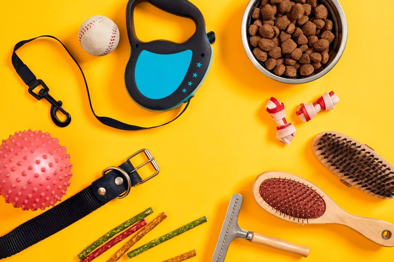 Dog food, toys, leash, brushes, and collar in front of a yellow background 