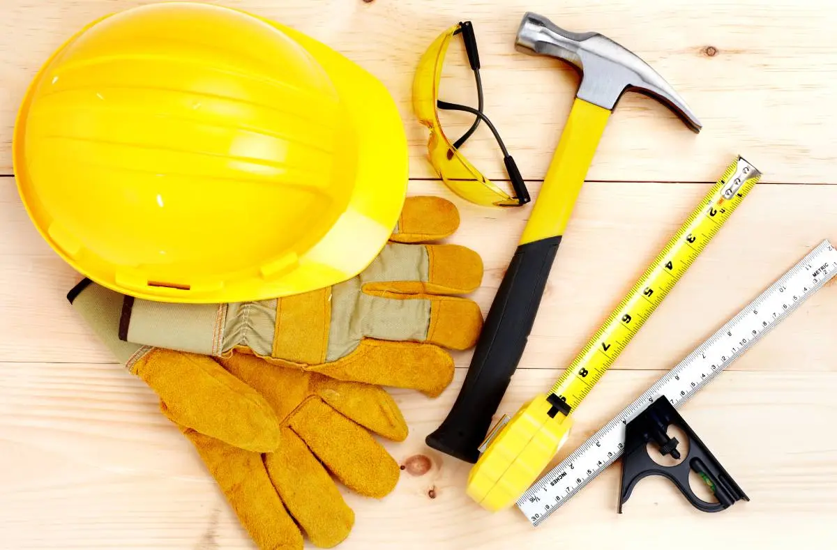 hardhat, measuring tape, hammer, goggles, and gloves laid out on a wooden table