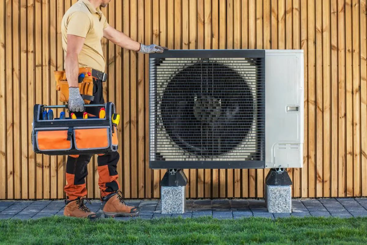 HVAC technician holding a toolbox and evaluating an HVAC system in front of a wood slat wall