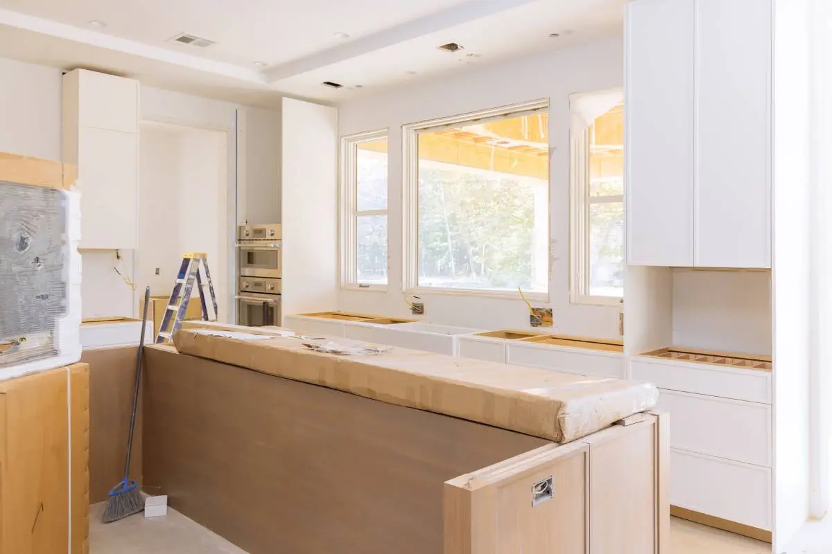 a kitchen layout being constructed with a broom, ladder, and other tools
