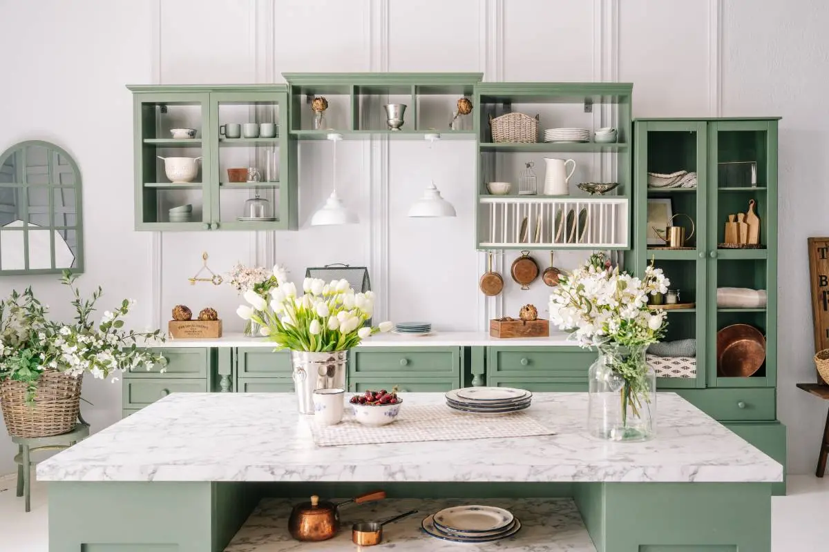 a marble countertop island with green cabinetry and flower arrangements 