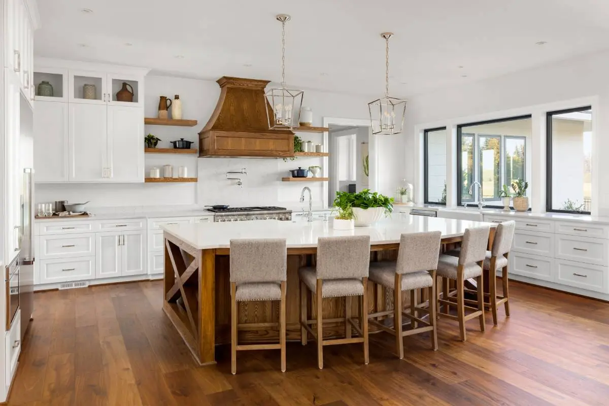 a large kitchen island with a marble countertop, statement overhead lighting, and white cabinets with gold accents