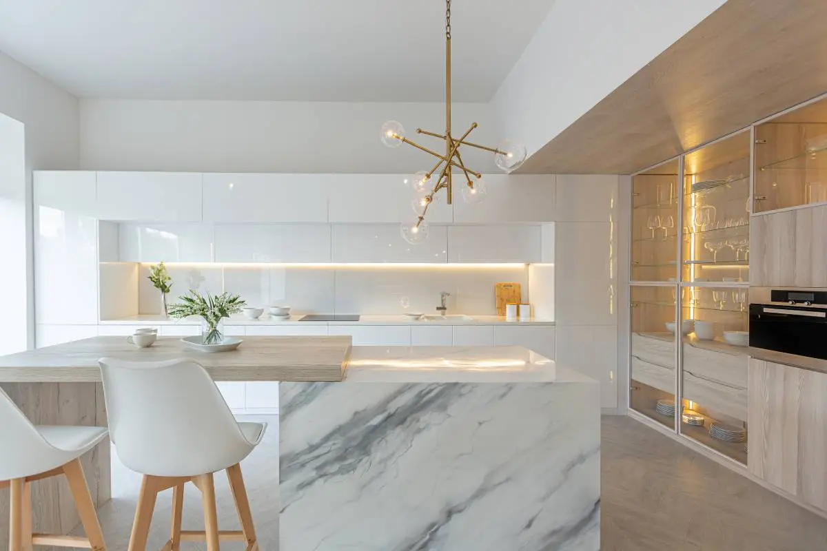 a sleek kitchen with a marble island, white cabinetry, and statement lighting