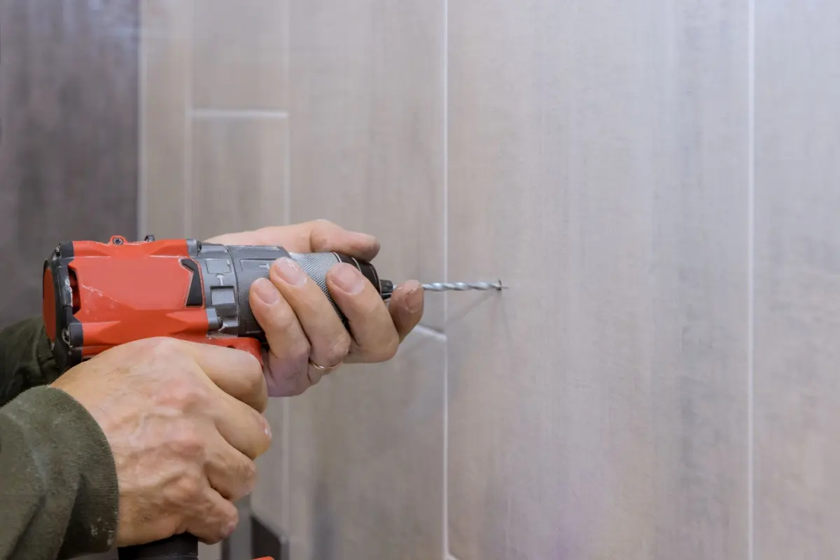 Plumber using power drill on inside of shower.