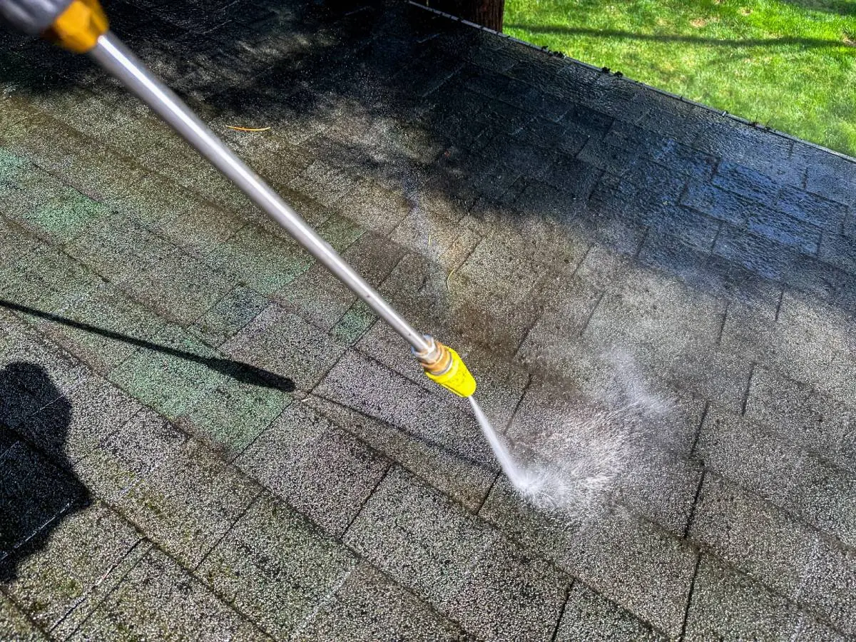 a roofing contractor power washing a roof during the spring with a lawn of green grass below