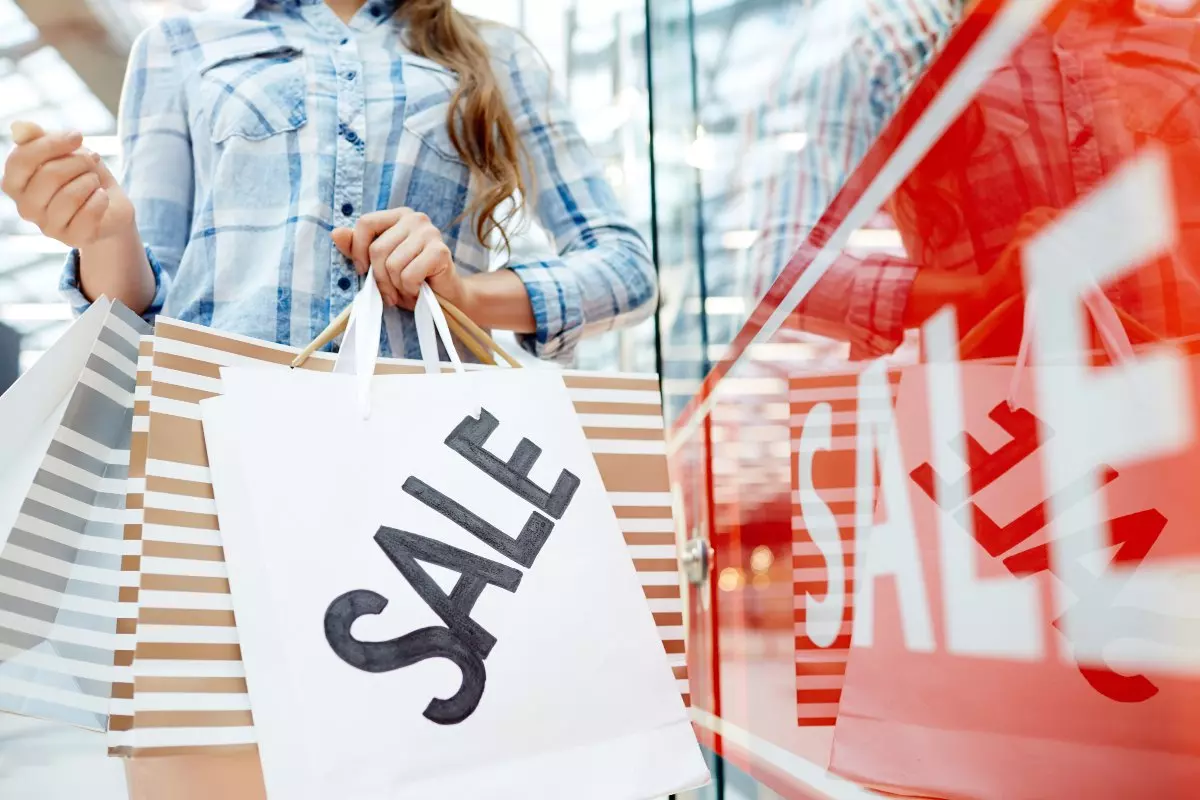 Close up on shopper carrying bag with "sale" written and standing next to a "sale" sign