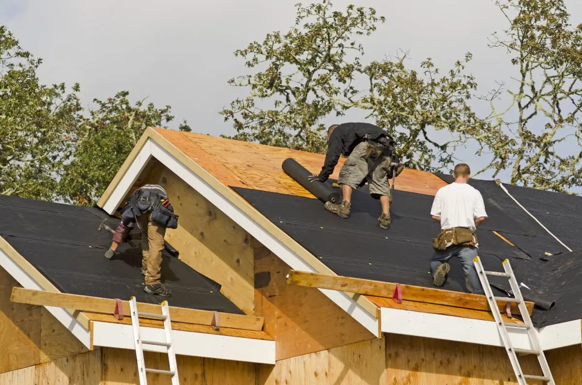 roofing crew working on a residential project with a gray sky and trees behind them