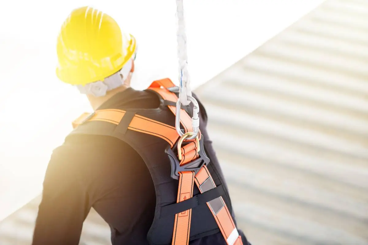 a roofer wearing a yellow hard hat and safety harness