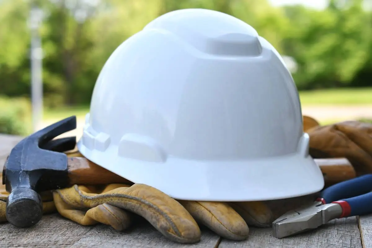 roofing tools including a white hard hat on work gloves, a hammer, and pliers