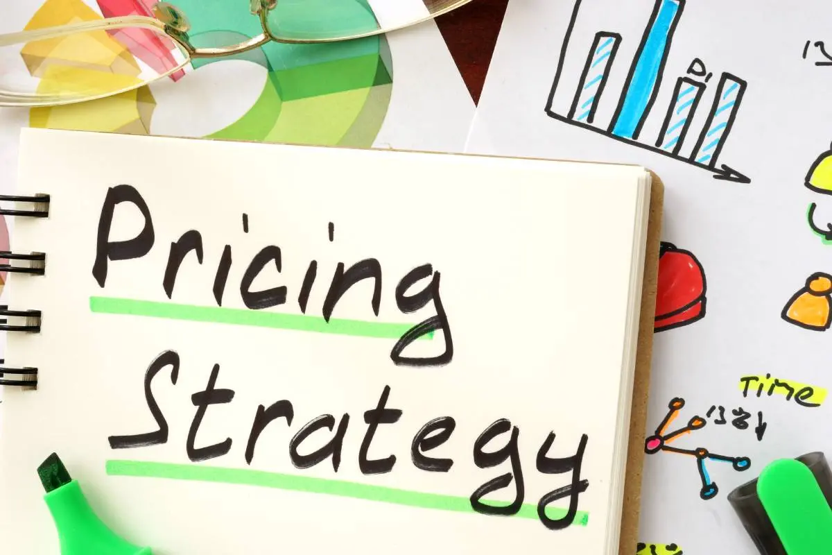 pricing strategy written and underlined with green highlighter on a notepad on top of colorful charts and graphs