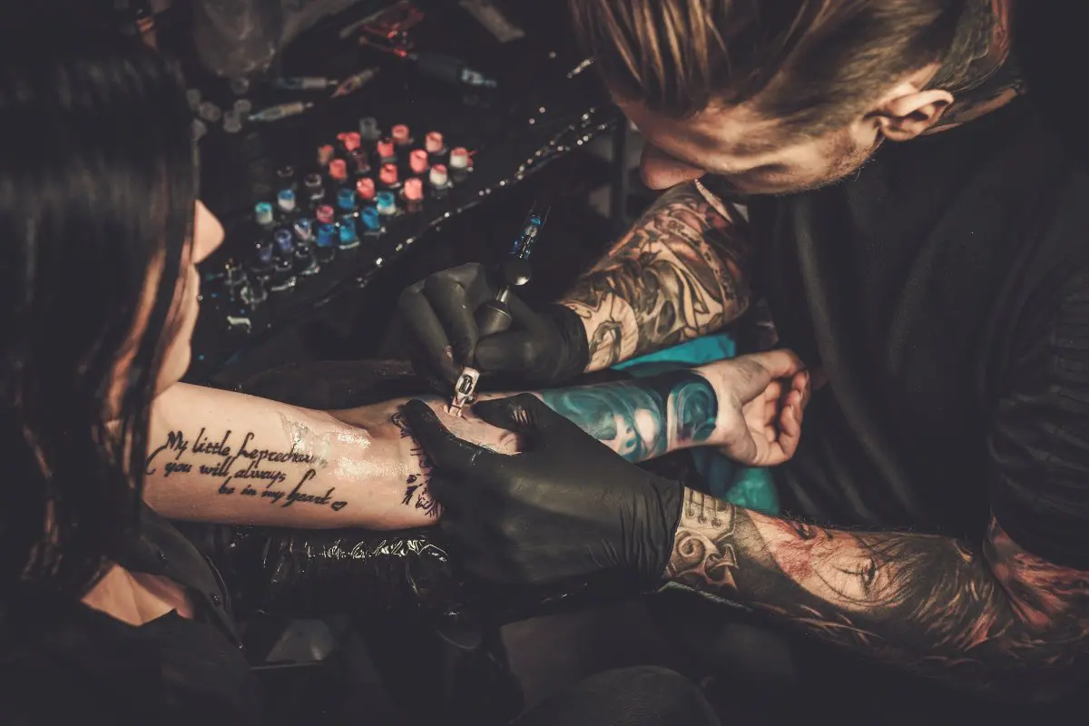 Tattoo artist tattooing client's arm